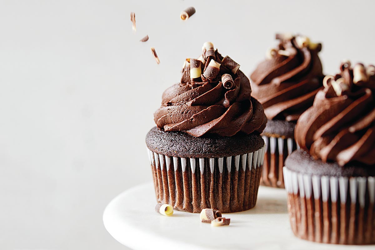 Chocolate cupcakes being topped with chocolate shavings