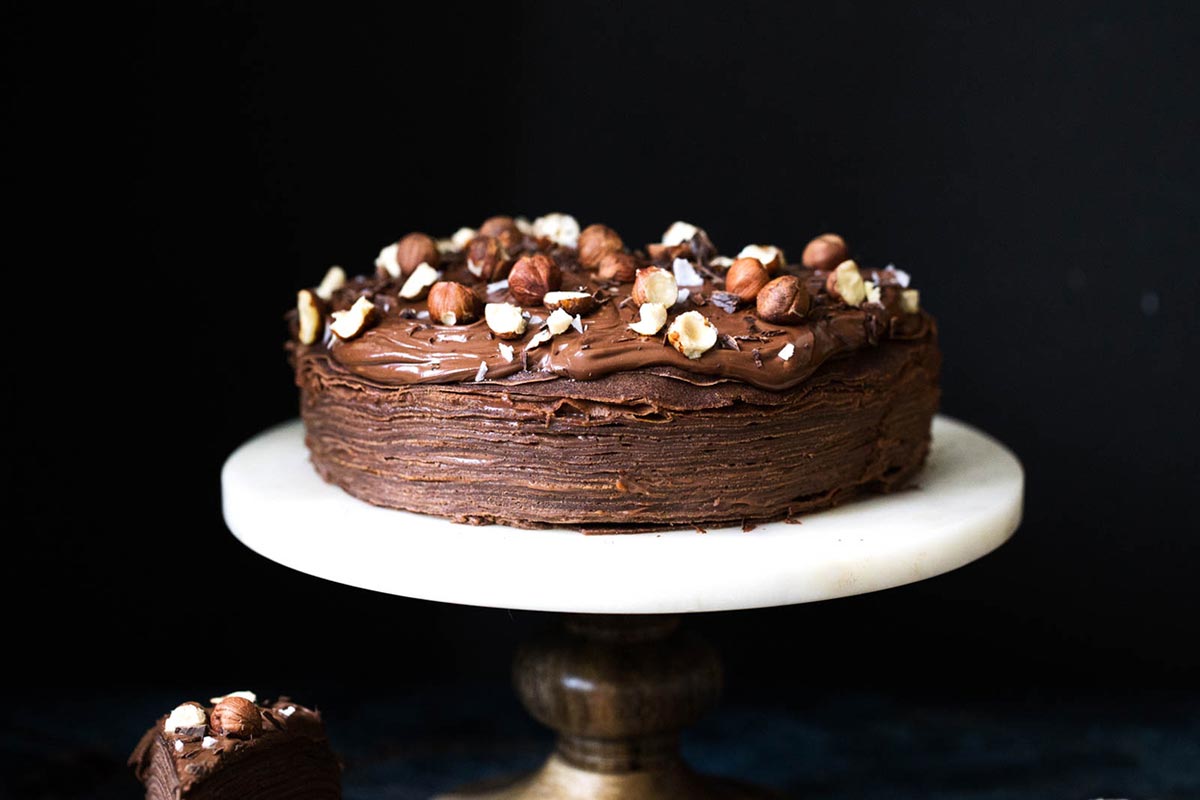 A chocolate crepe cake filled with chocolate hazelnut spread with a slice removed