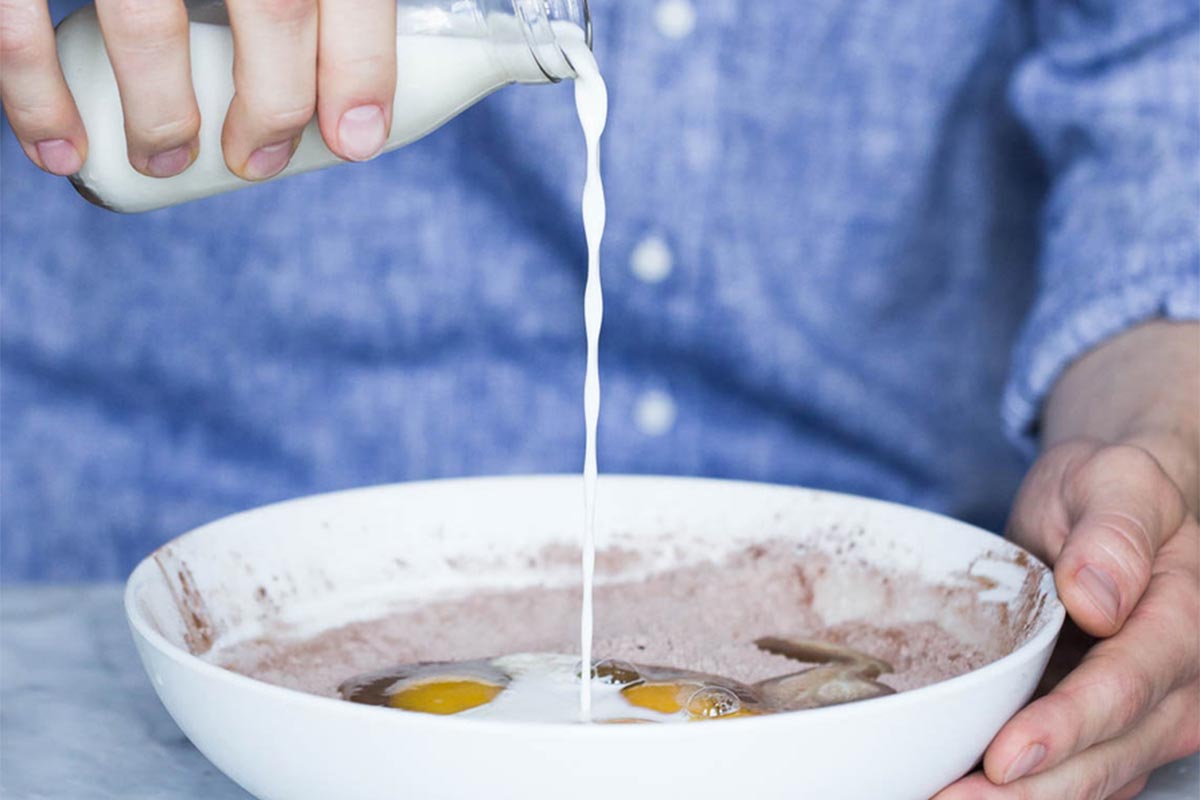 A baker pouring milk into a bowl of crepe batter