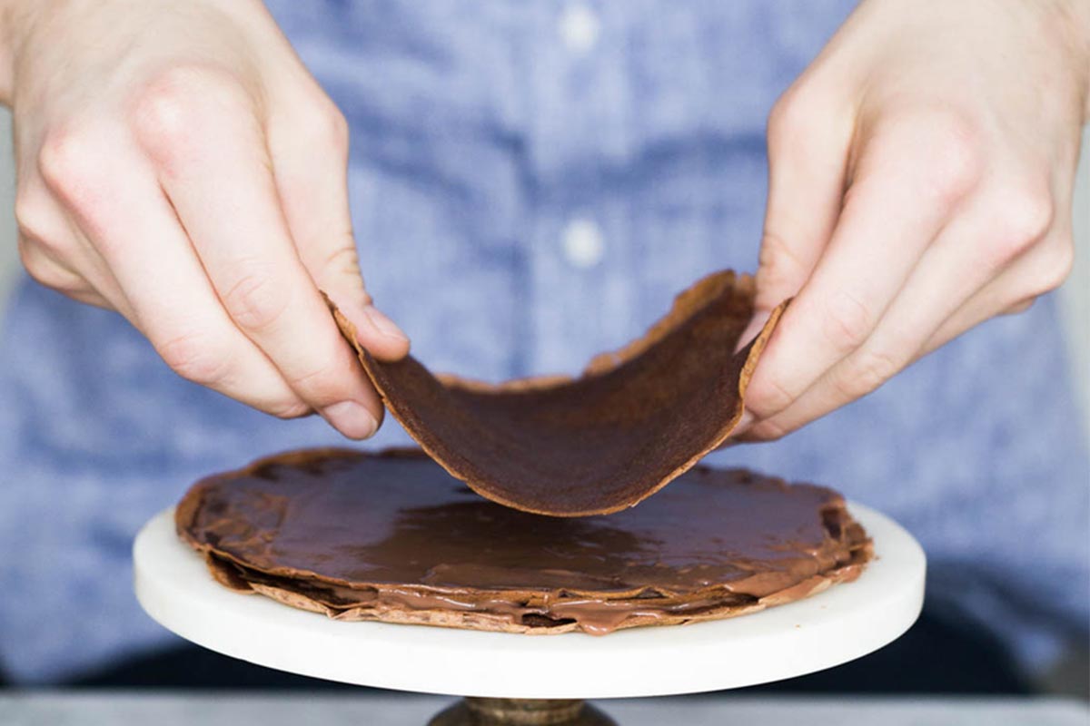 A baker stacking chocolate crepes on top of each other to form a cake