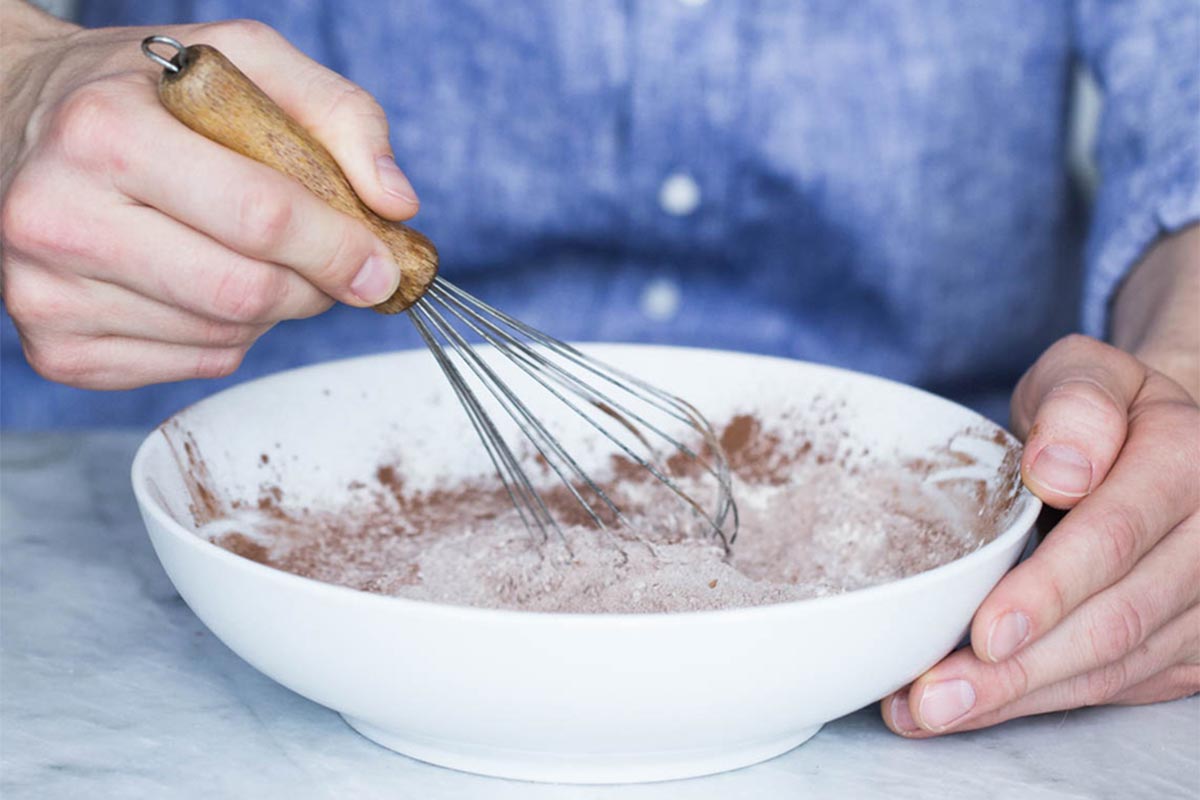 A baker whisking together flour and cocoa powder in a bowl