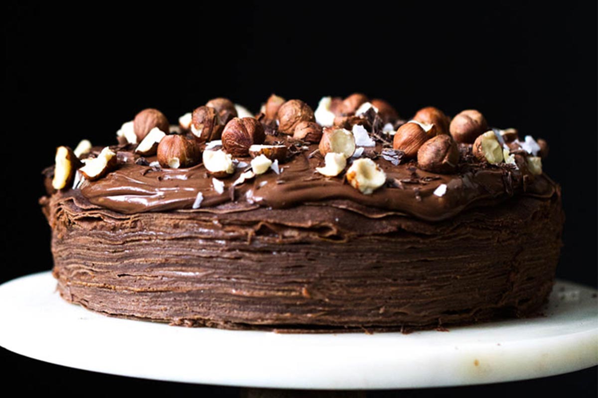 Chocolate crepe cake on a plate topped with hazelnuts 