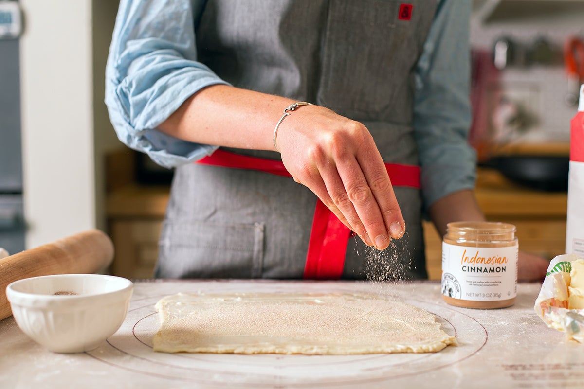 A baker sprinkling cinnamon-sugar over rolled out pie dough