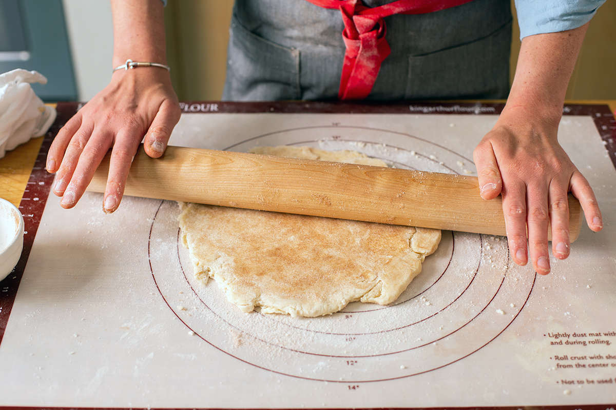 A baker rolling out pie dough with cinnamon-sugar sprinkled on top