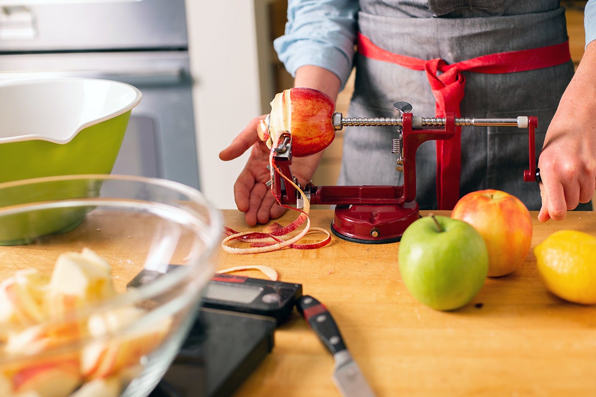 A baker using an apple peeler and corer to prep apple for pie baking