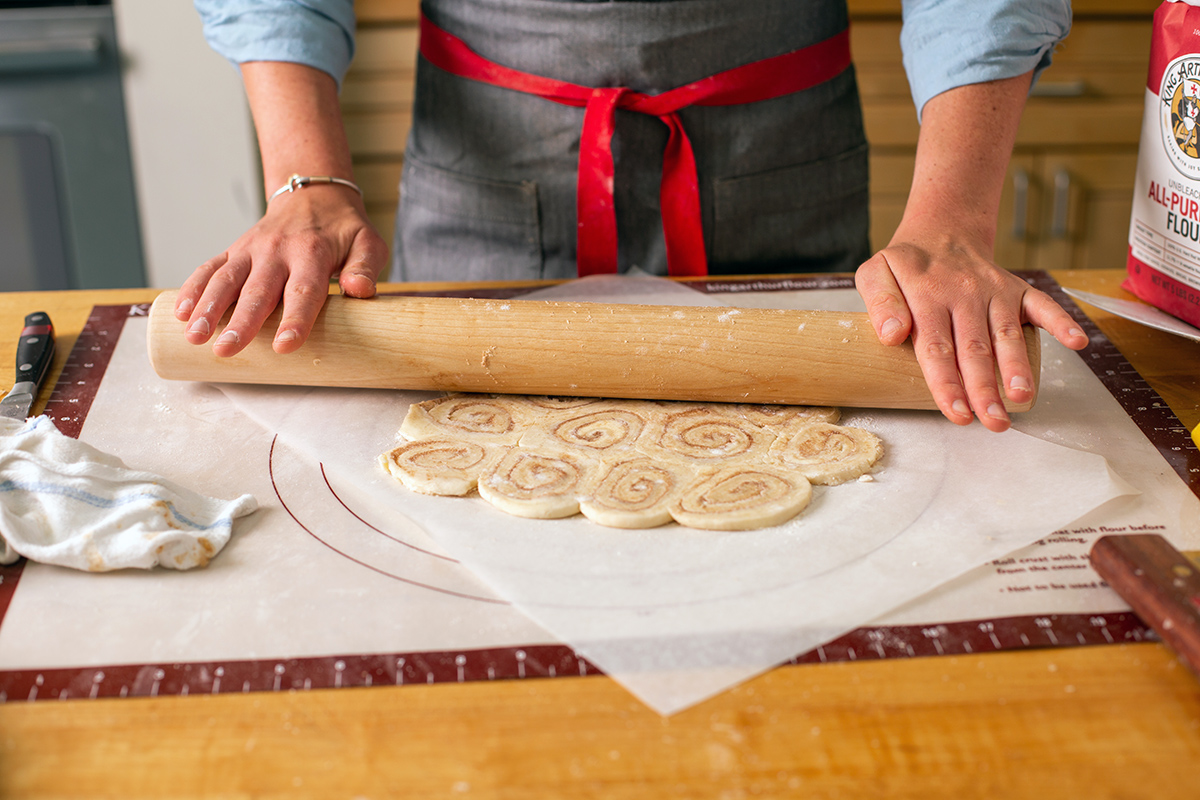 A baker rolling out cinnamon bun pie crust to place on top of an apple pie
