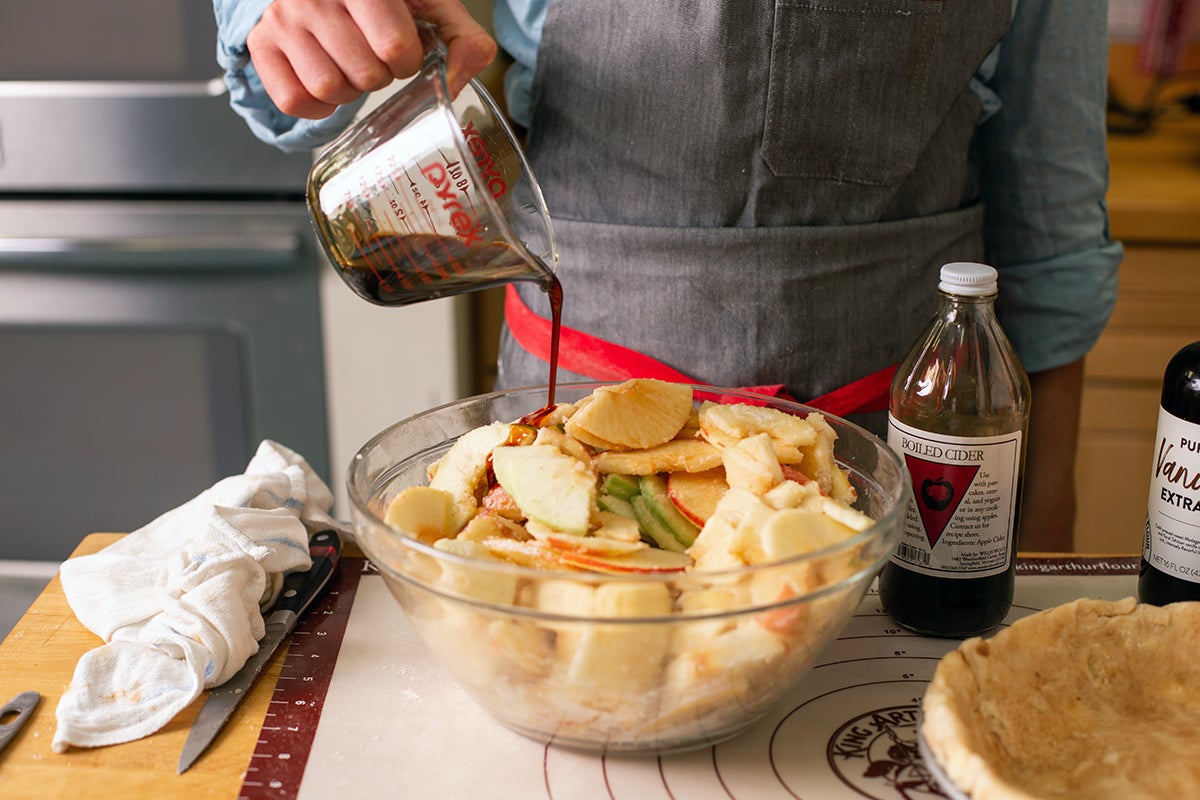 A baker pouring boiled cider into a bowl of apples for apple pie