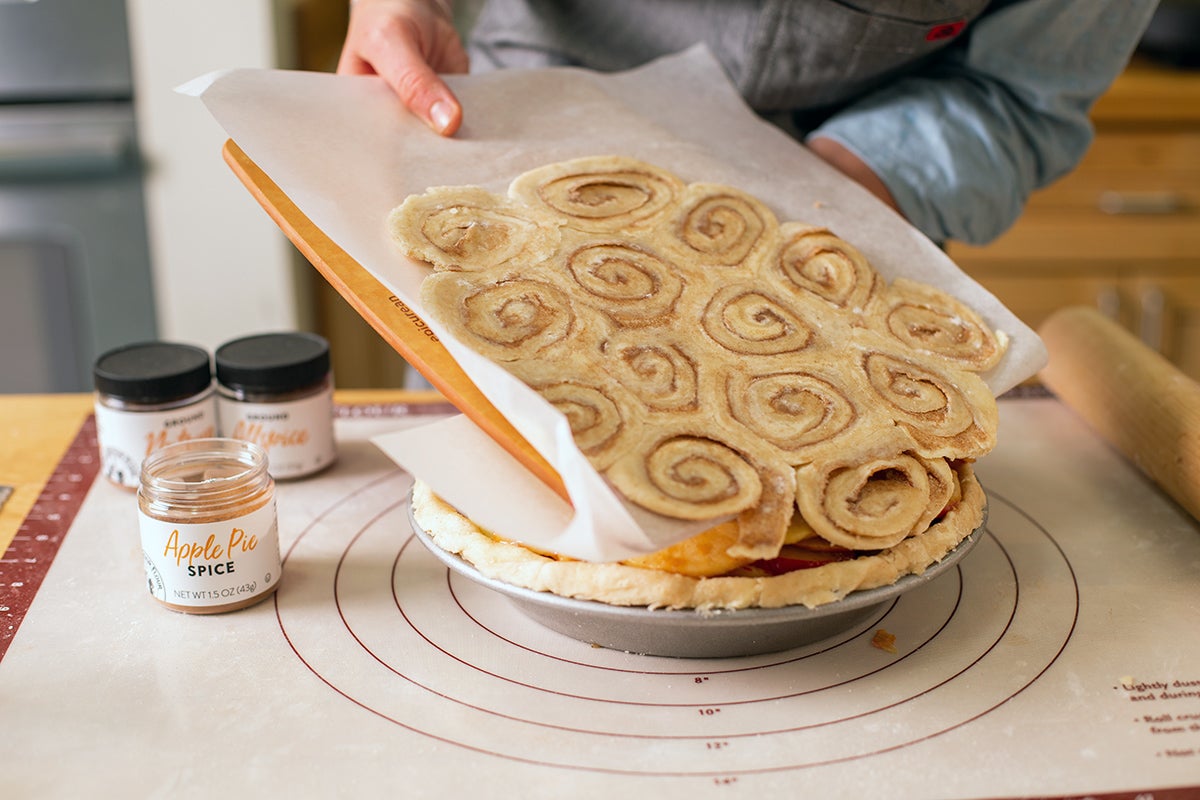 A baker transferring a cinnamon bun pie crust to an apple pie