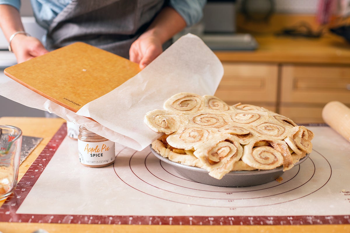 A baker transfering a cinnamon bun pie crust to the top of an apple pie