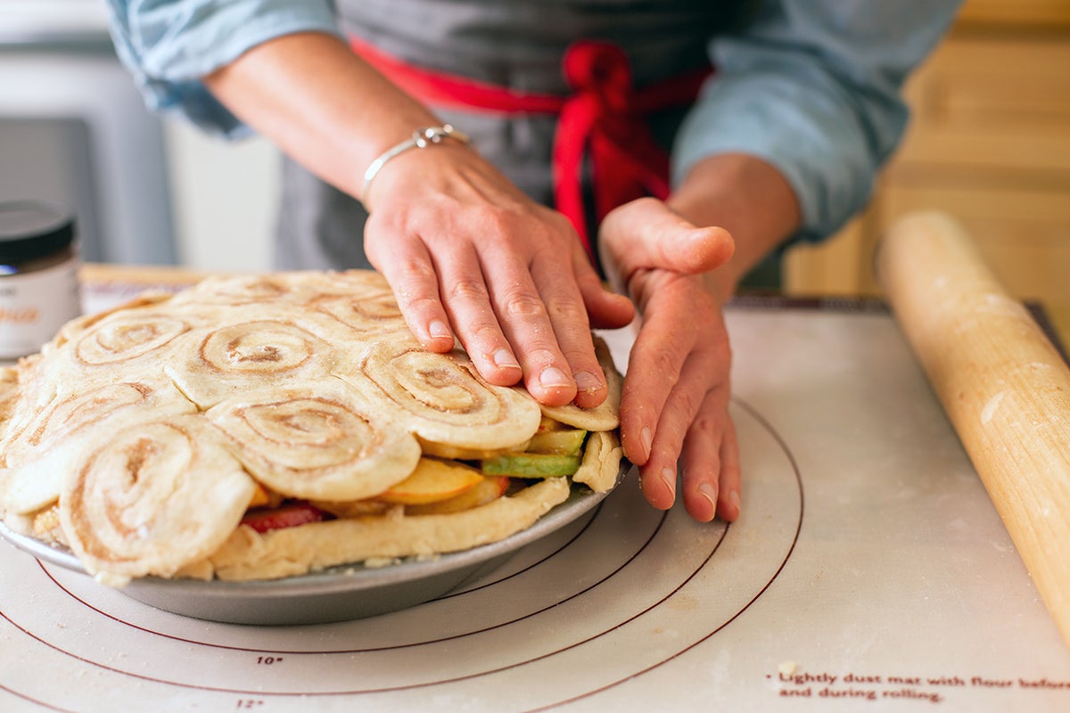 A baker putting final touches on a cinnamon bun apple pie top crust