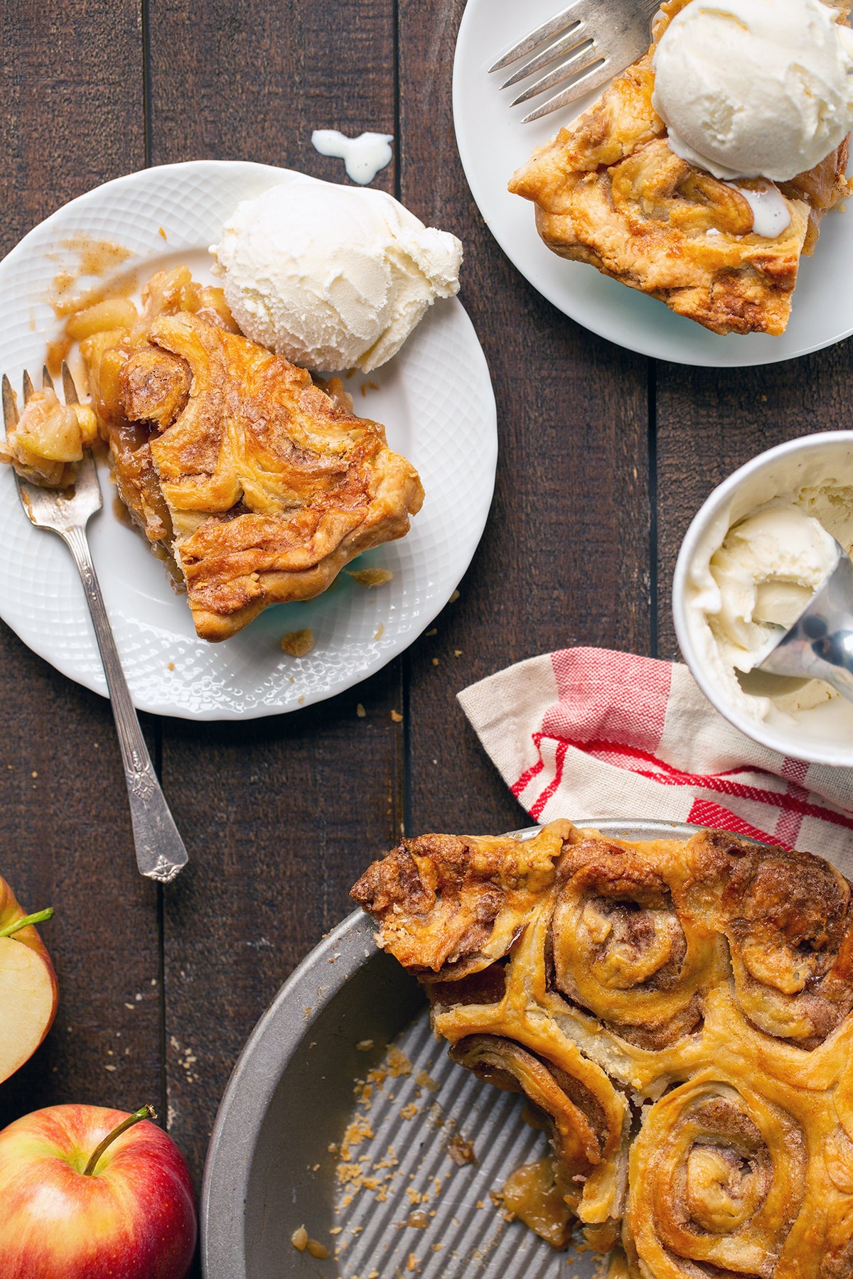 A cinnamon bun apple pie with a few slices on plates served à la mode