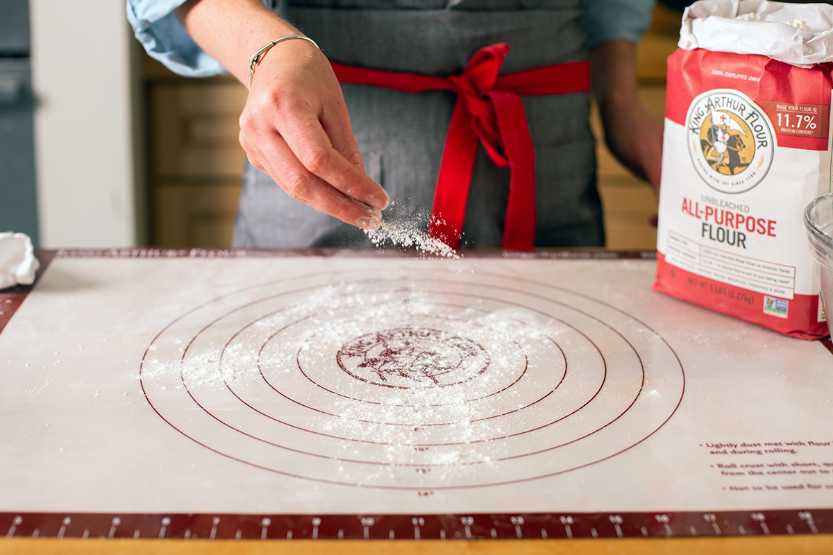 A baker dusting a rolling mat with flour