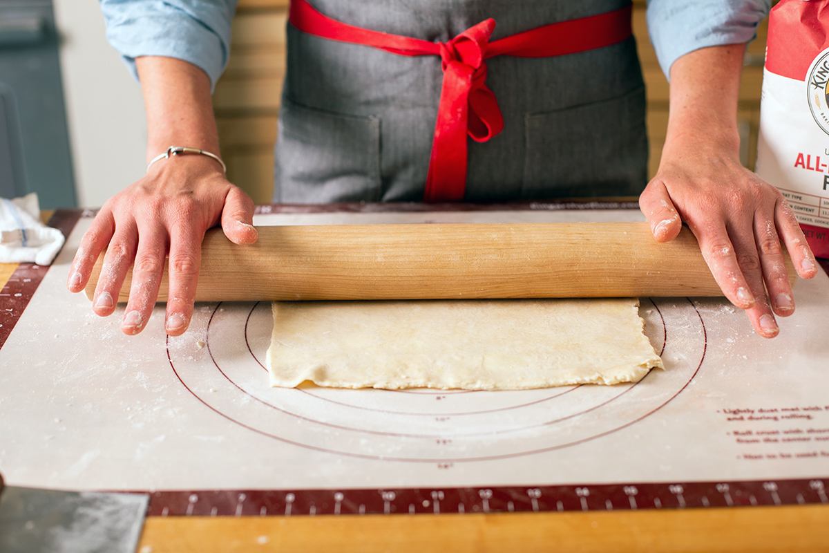 A baker rolling out pie dough into a rectangle