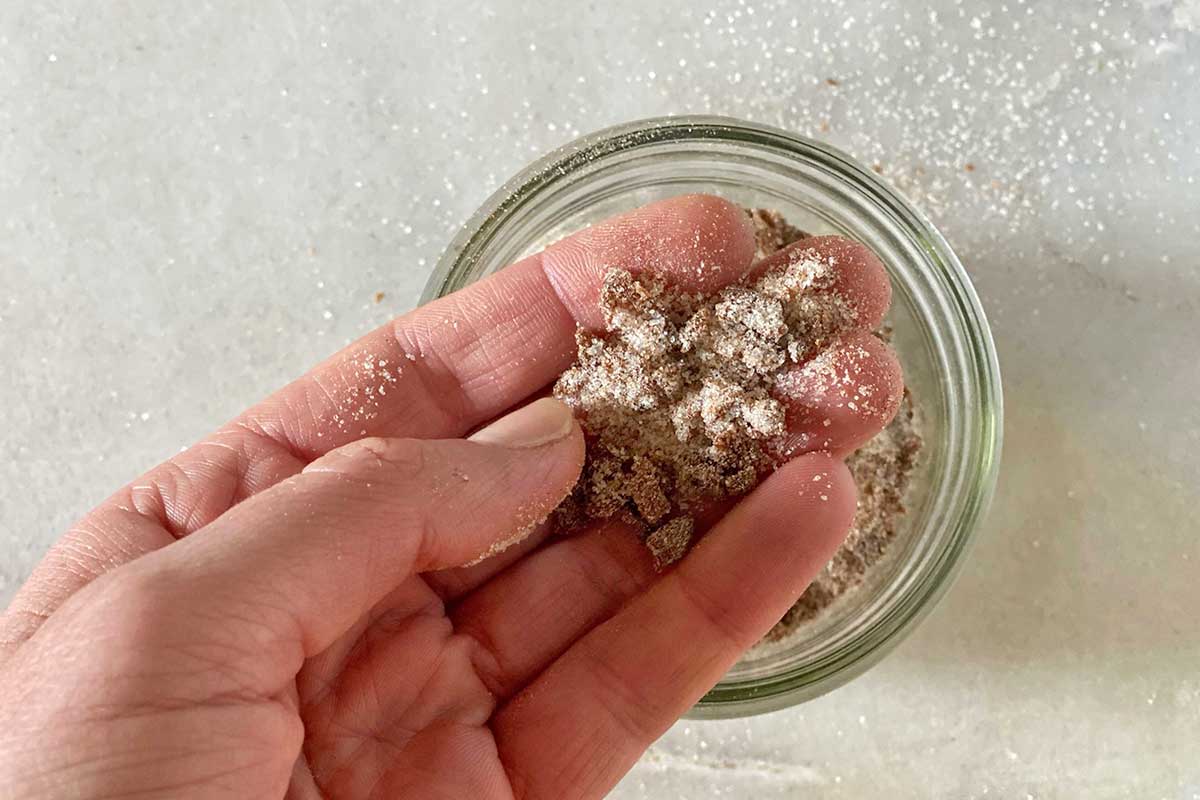 A baker's hand showing the texture of the cinnamon filling to the camera: it looks like rough sand with a few chunks of raisins