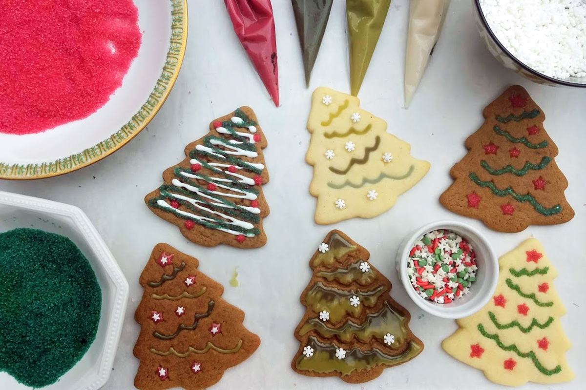 Bowls of natural sprinkles and bags of icing next to Christmas tree-shaped cookies
