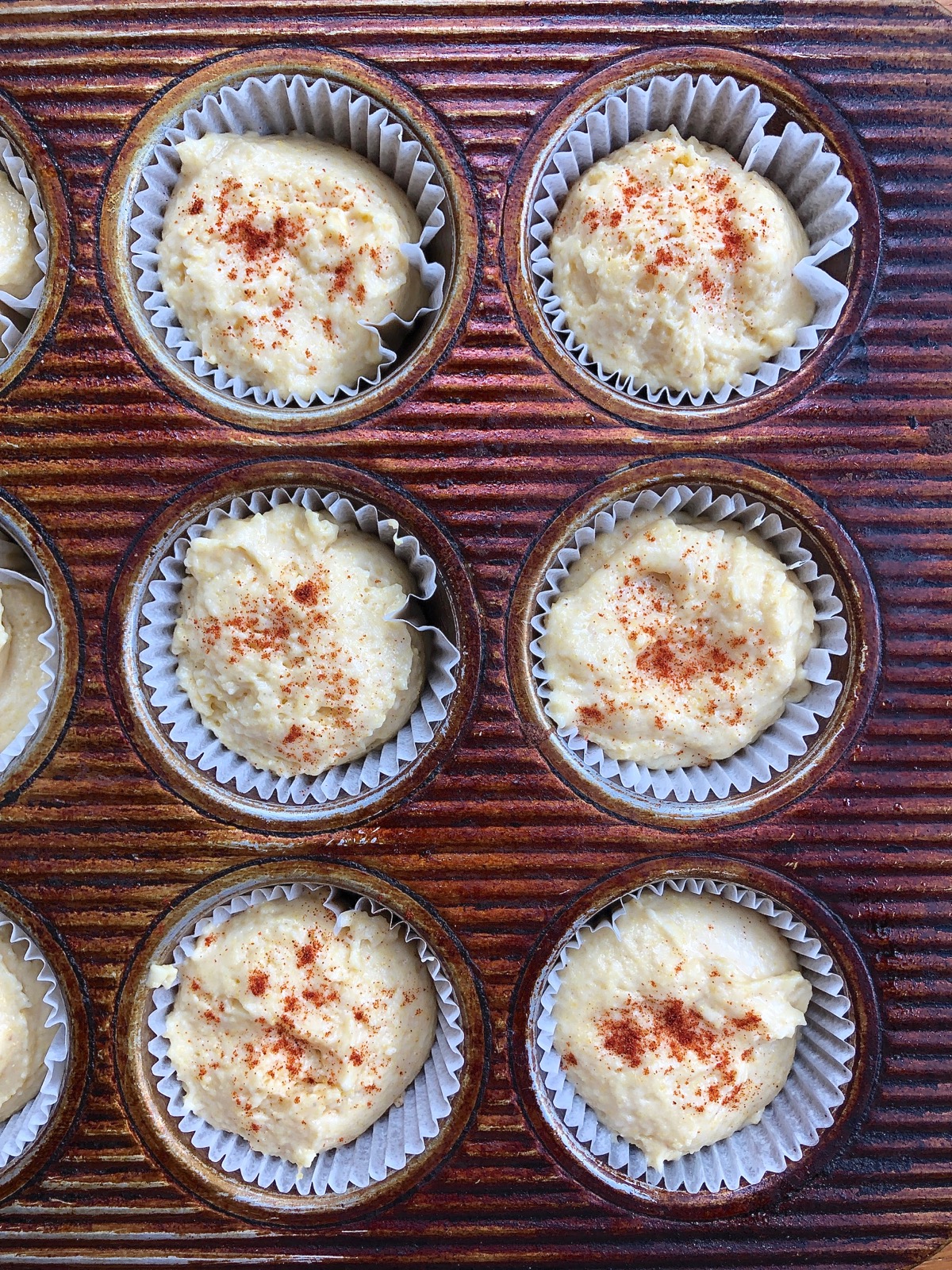 Corn muffins in a muffin tin sprinkled with paprika, ready to be baked