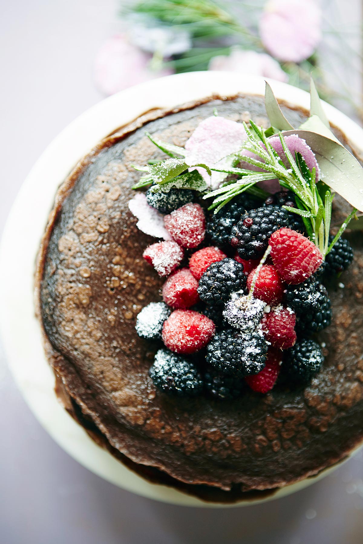 A chocolate crepe cake topped with fresh berries and confectioners' sugar