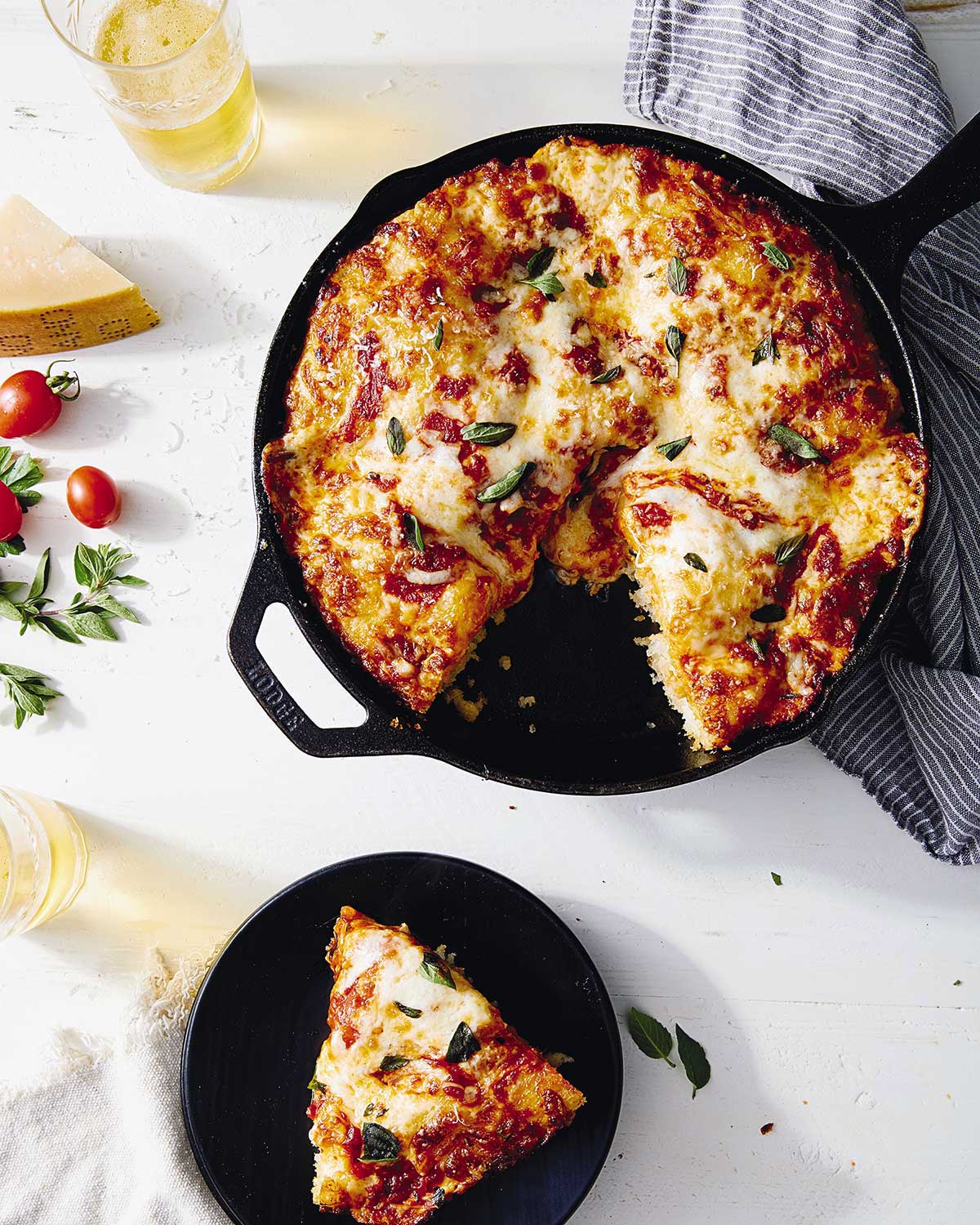 Crispy Cheesy Pan Pizza in a cast iron pan topped with cheese, tomato sauce, and fresh herbs