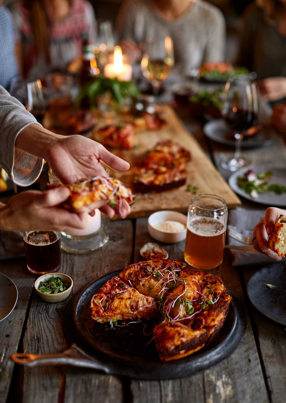 An evening dinner scene with a cast iron pan pizza at the center of the table surrounded by people