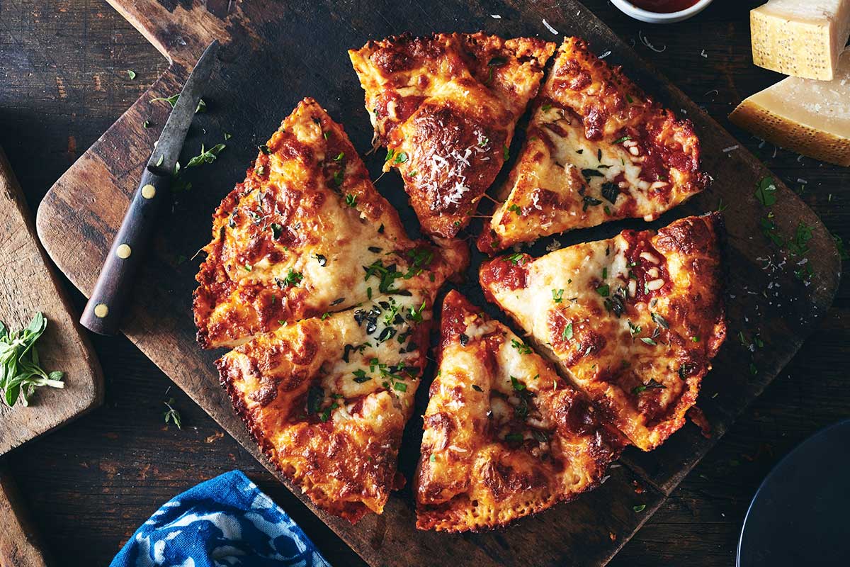 Cast iron pan pizza on a cutting board cut into slices on a bread board