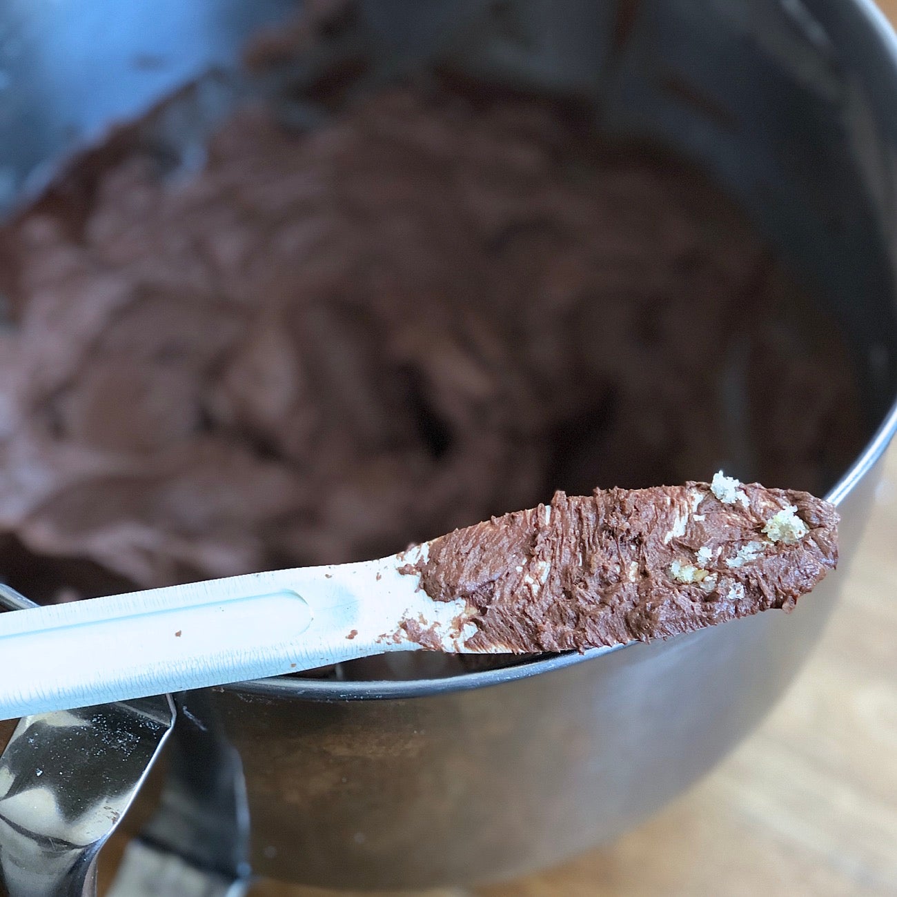 Spatula with frosting and crumbs sitting atop a large bowl of chocolate frosting.