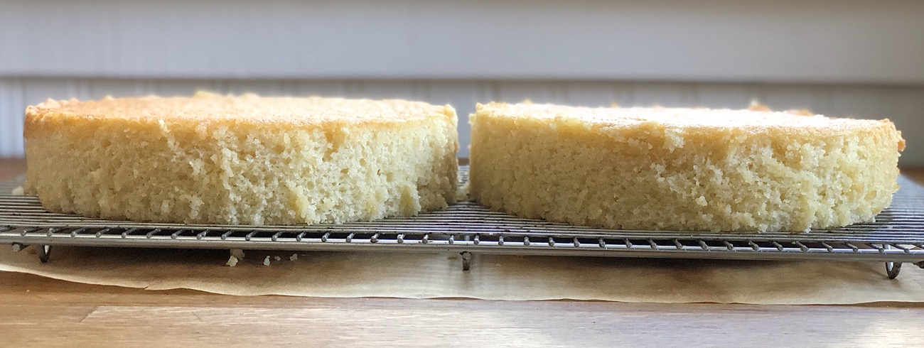Two cake layers on a cooling rack, side by side, waiting to be frosted.