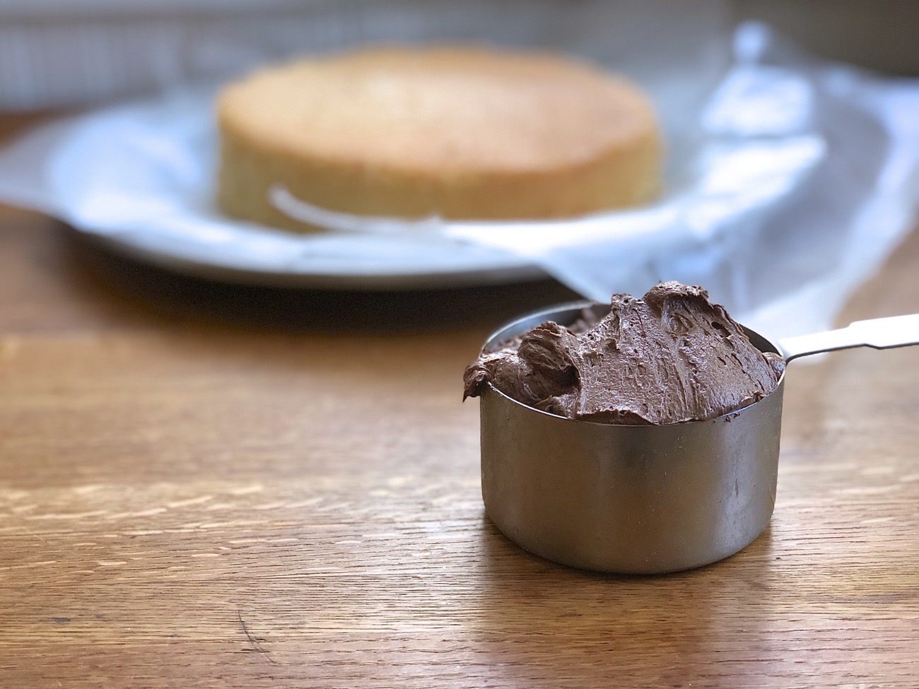A 1-cup measure of chocolate frosting ready to be spread onto a layer cake.