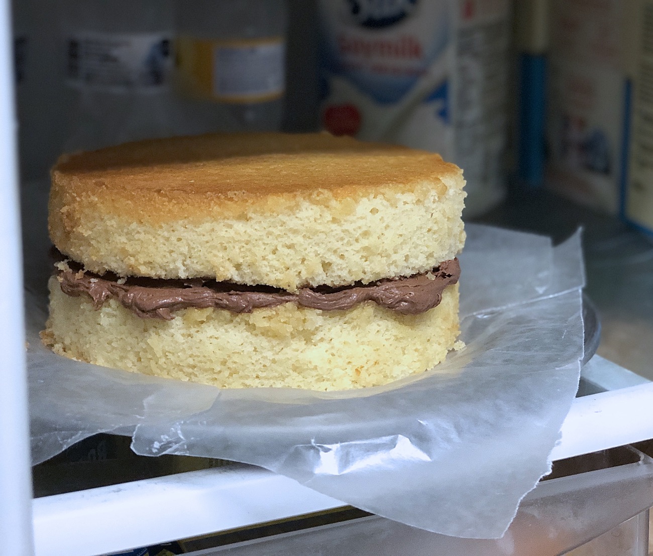 Unfrosted double-layer yellow cake, chocolate frosting in the middle, chilling in the refrigerator.