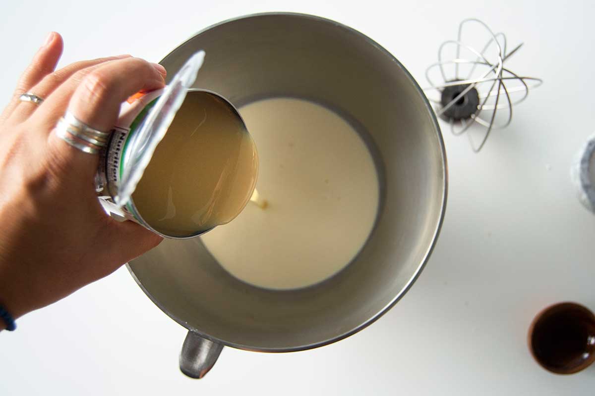 Sweetened condensed milk being poured into the bowl of a stand mixer