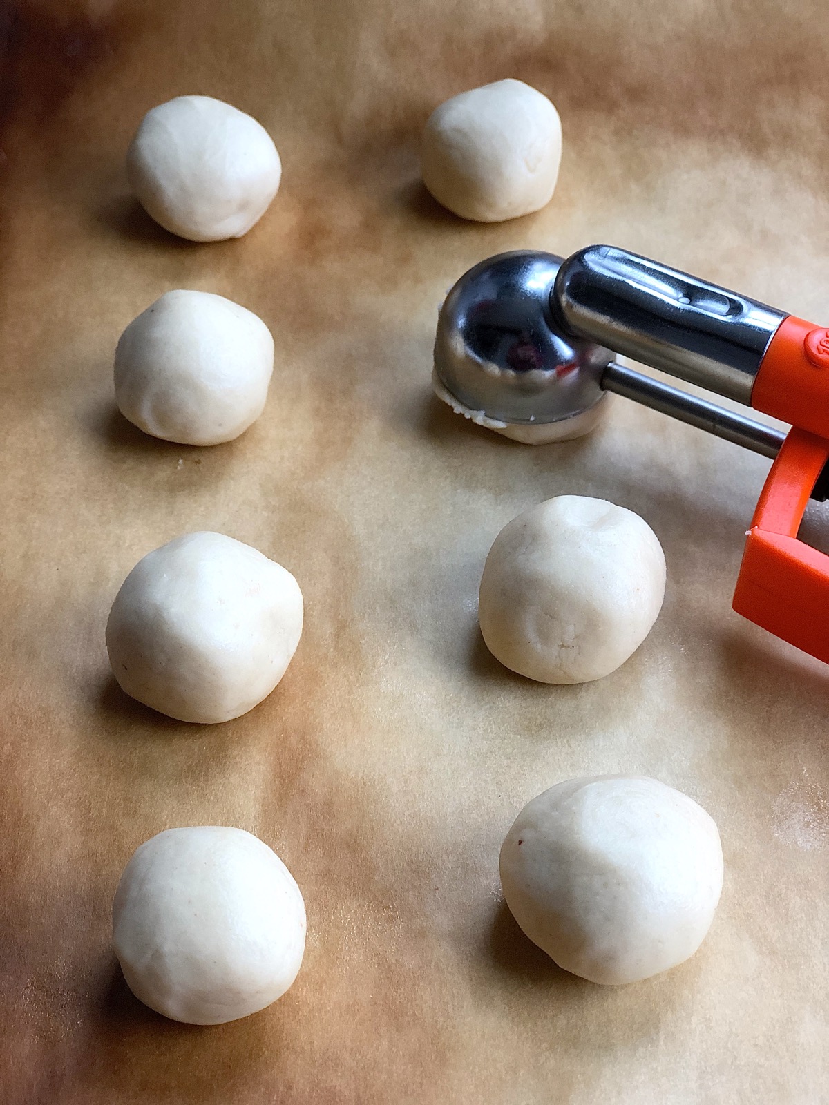 Balls of shortbread cookie dough on a baking sheet with a cookie scoop; cookies ready to be flattened.