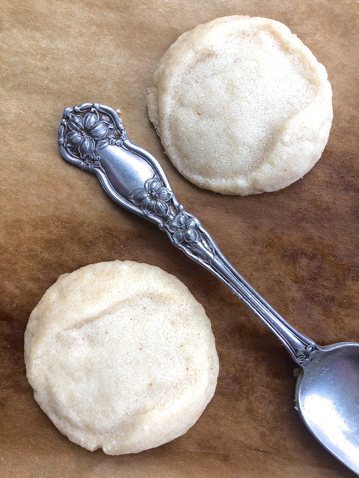 Two baked shortbread cookies with only a vague imprint, shown with the scrolled spoon handle that made the imprint.