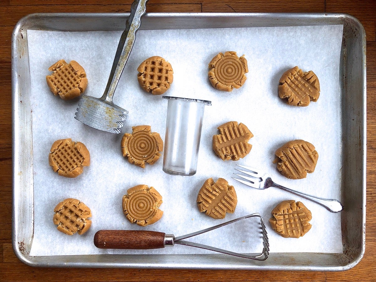 Baking sheet with balls of cookie dough, flattened with various tools, ready to bake.