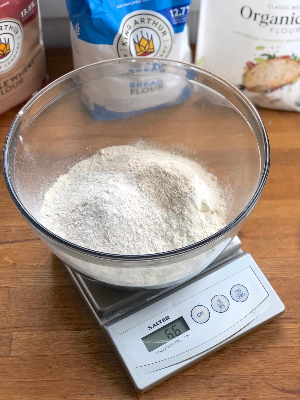 Bowl of flour on a scale, bags of flour in the background.