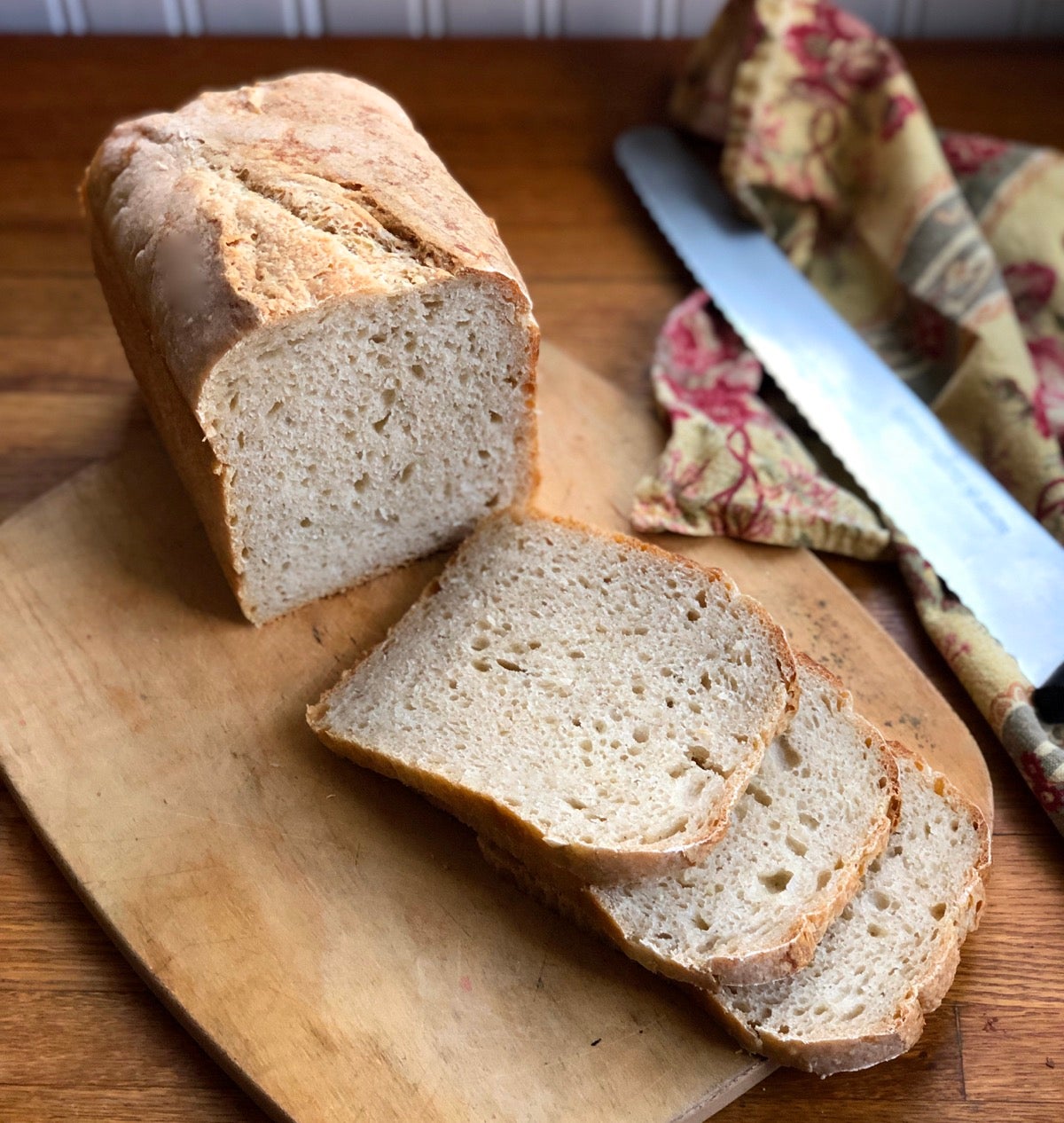 Loaf of sourdough bread on a cutting board with three slices fanned out; knife and napkin on the side.