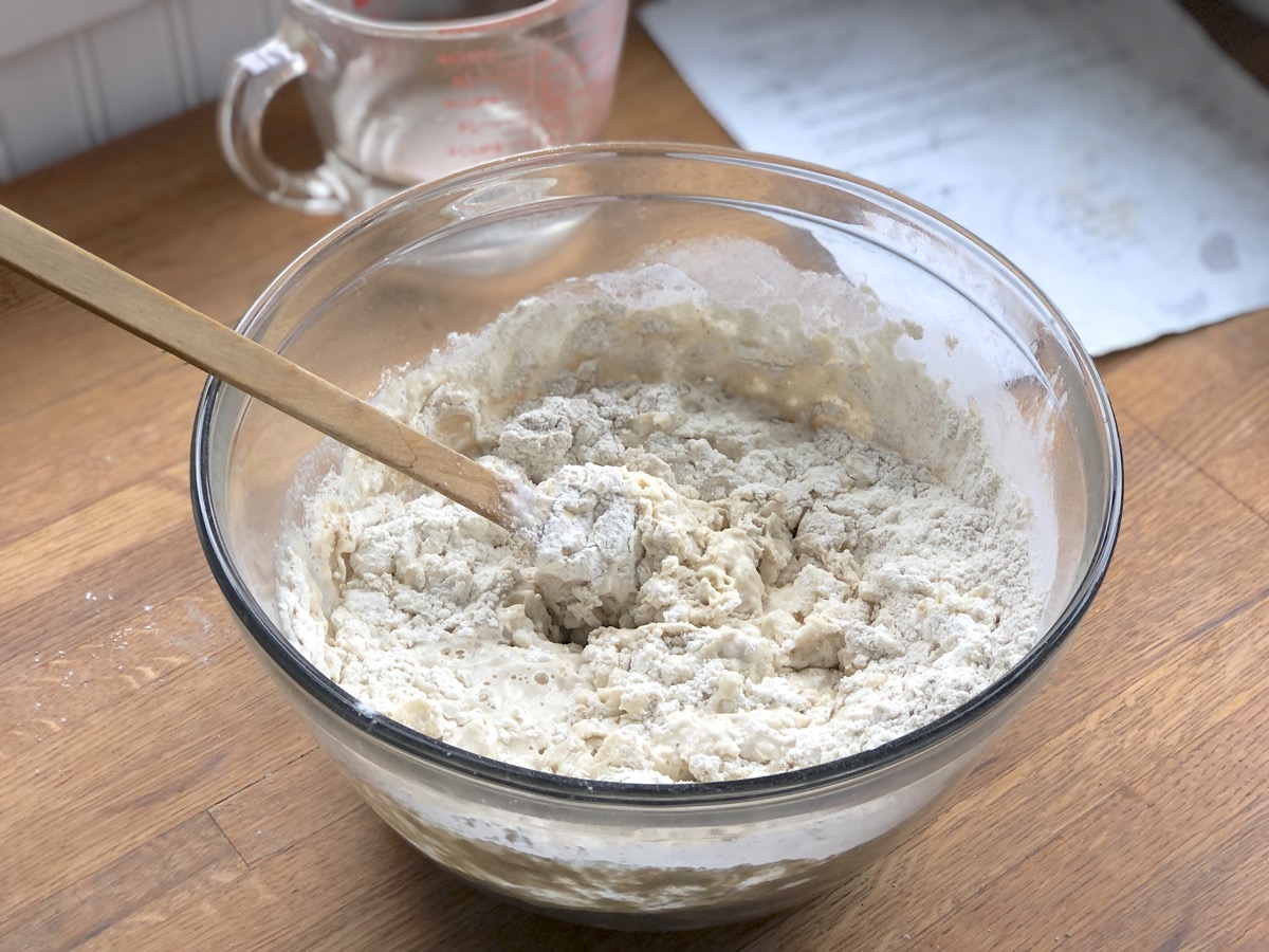 Sourdough bread ingredients in a bowl being stirred with a rubber spatula.