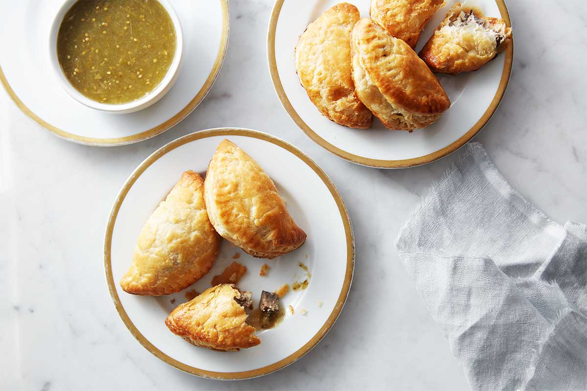 Two plates of empanaditas next to a bowl of dipping sauce