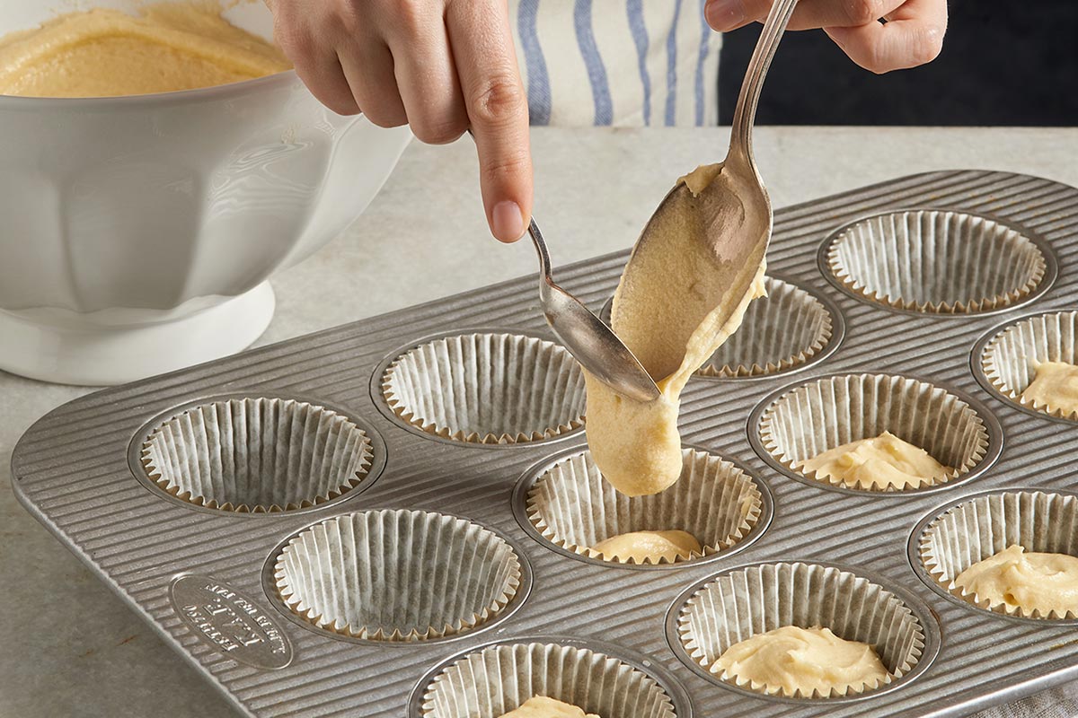 A baker pouring cake batter into a muffin pan