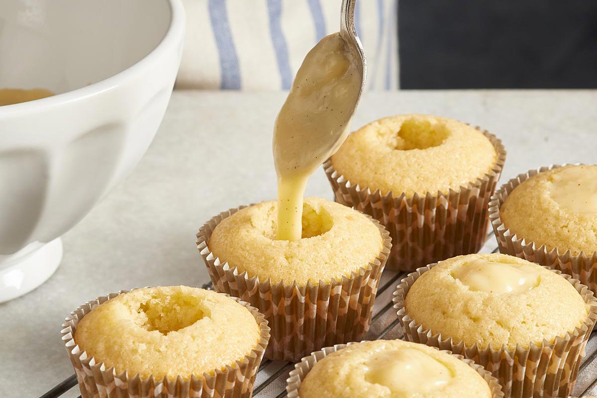 Cored cupcakes being filled with pastry cream