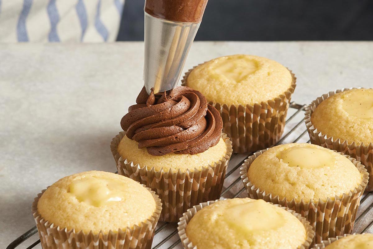 Yellow cupcakes being topped with chocolate frosting