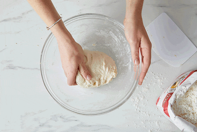A baker folding crispy cheesy pan pizza dough in a bowl