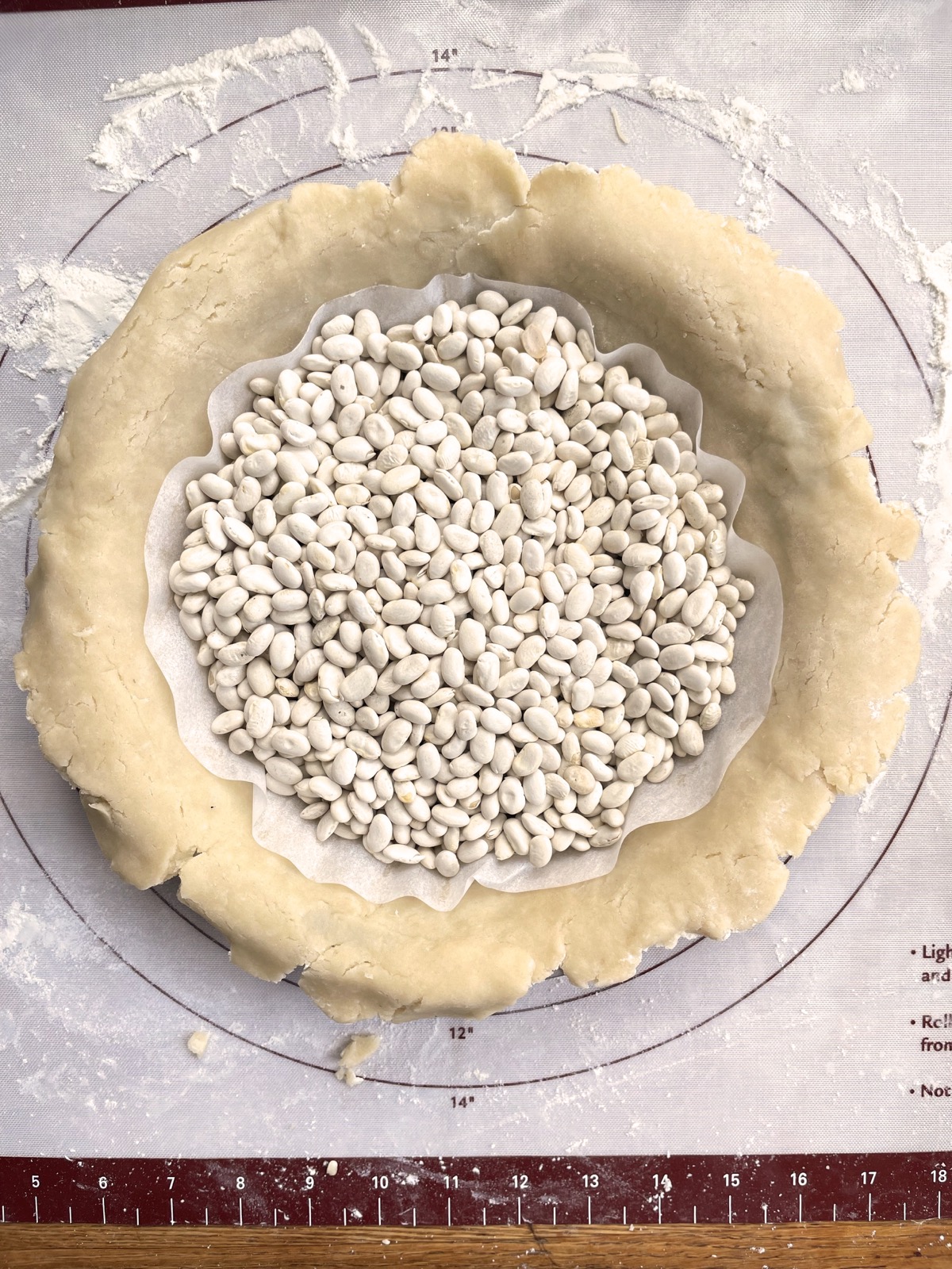 Pie crust in a pan layered with a parchment circle and dried beans, ready to prebake.
