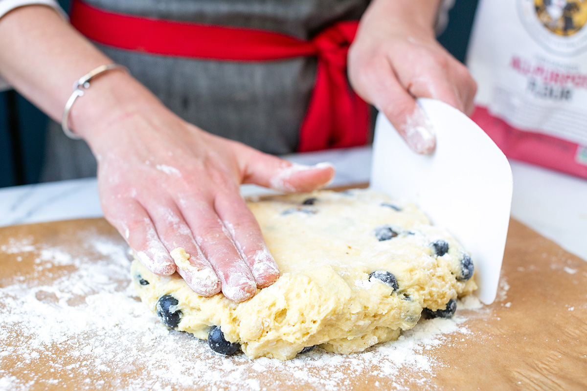 A baker using a dough scraper to pat out scone dough into a 1/2"-thick rectangle
