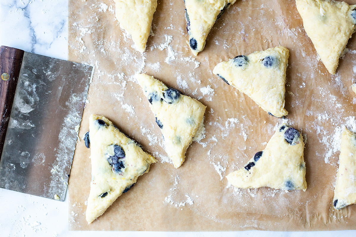 A bench knife next to a tray of shaped, unbaked blueberry scones
