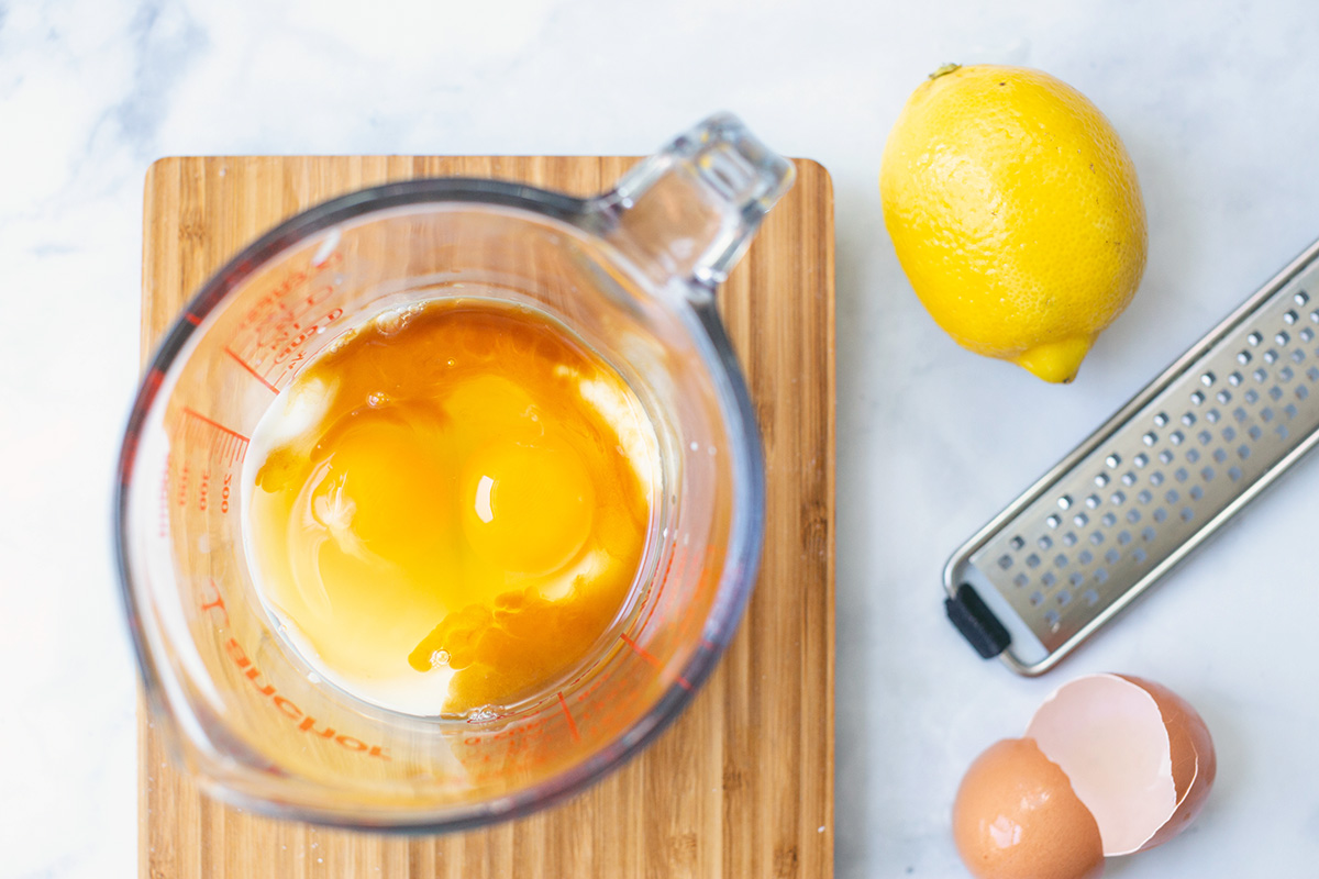 Two eggs cracked into a measuring cup on a scale next to a lemon and a zester