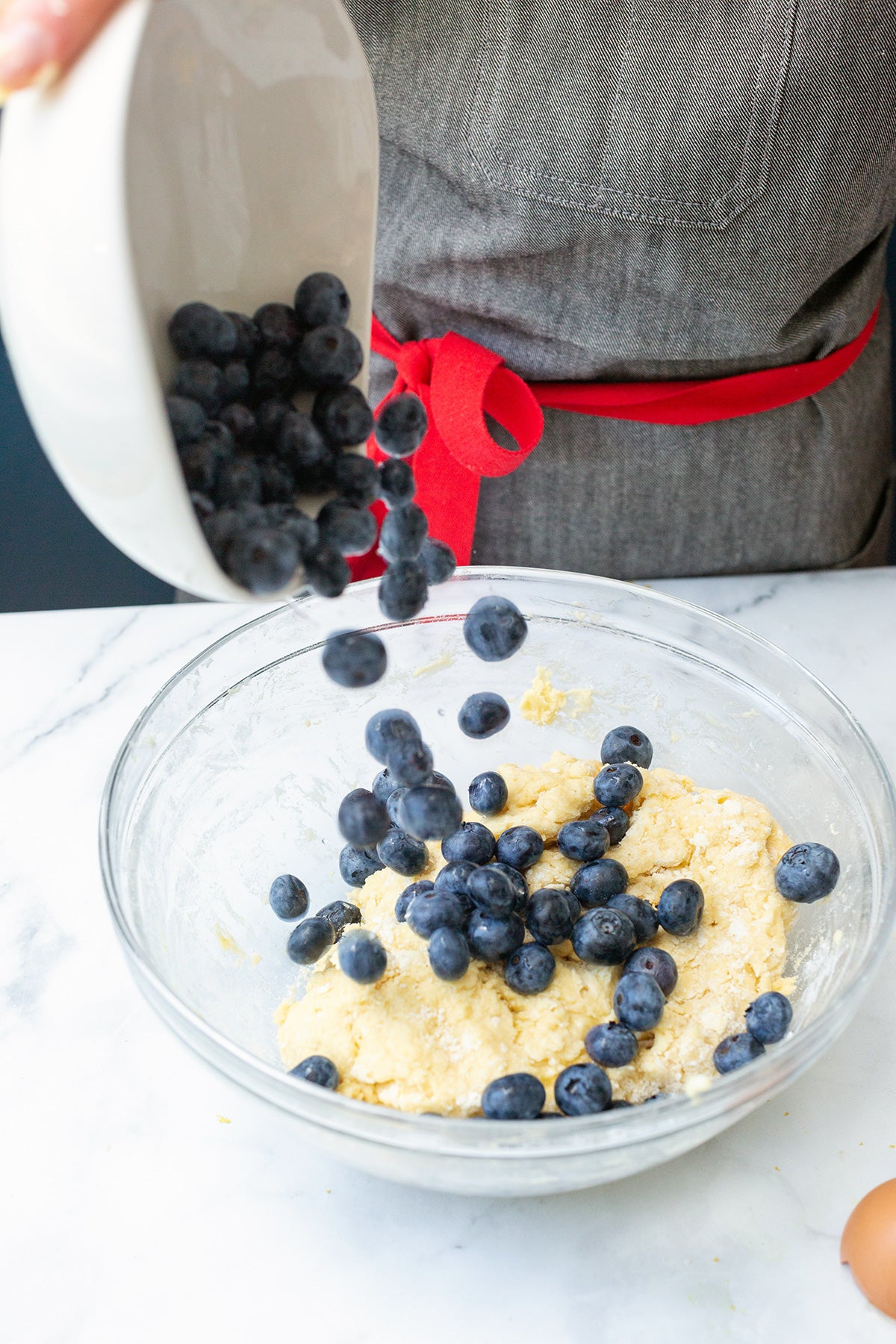 A baker pouring a bowl of fresh blueberries into scone dough