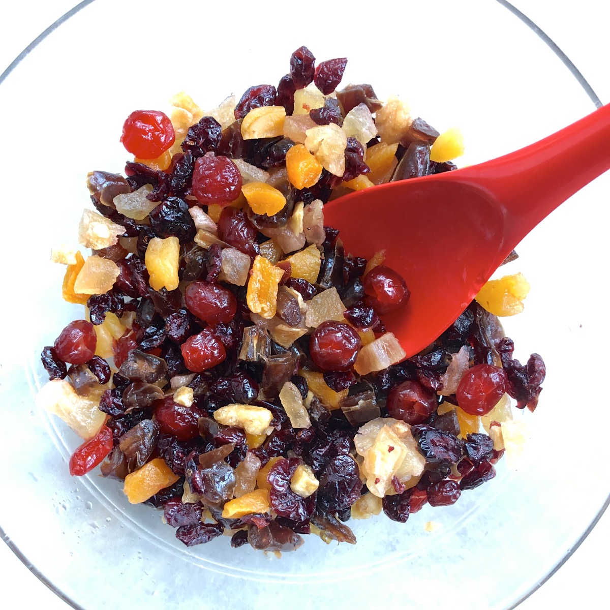 Choped dried fruit moistened with cranberry juice in a large bowl with a red spoon.