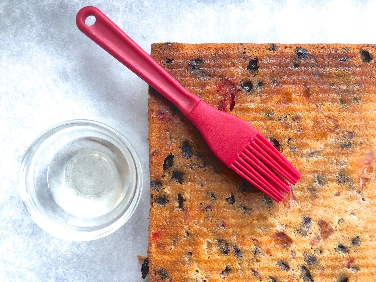 Warm fruitcake bars being brushed with vanilla syrup.