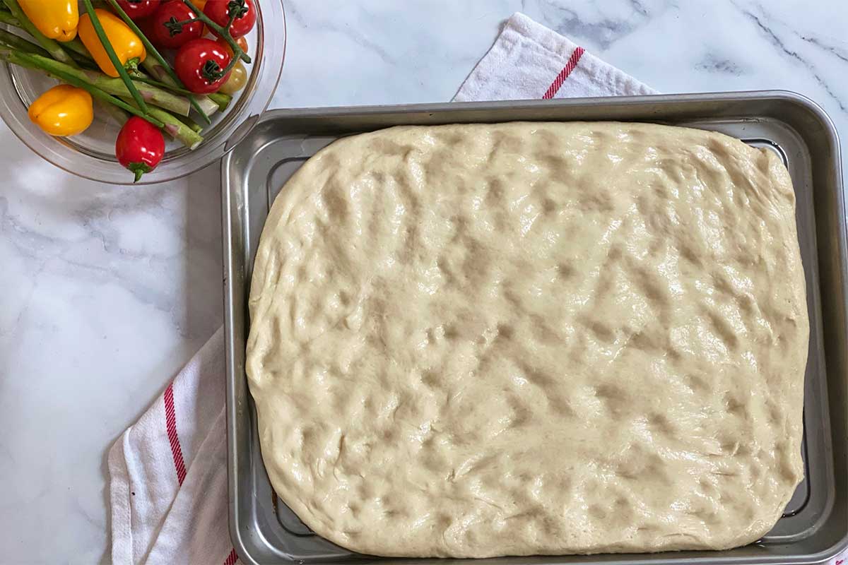 Focaccia dough on a baking sheet, ready to be topped and baked