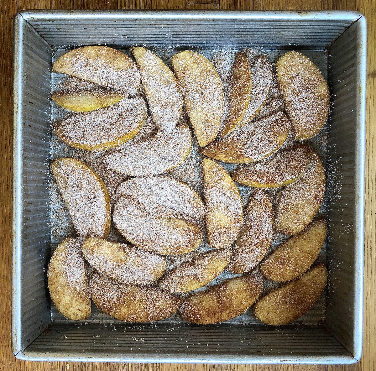 Apple slices tossed with cinnamon and sugar, arranged in the bottom of a 9" square pan