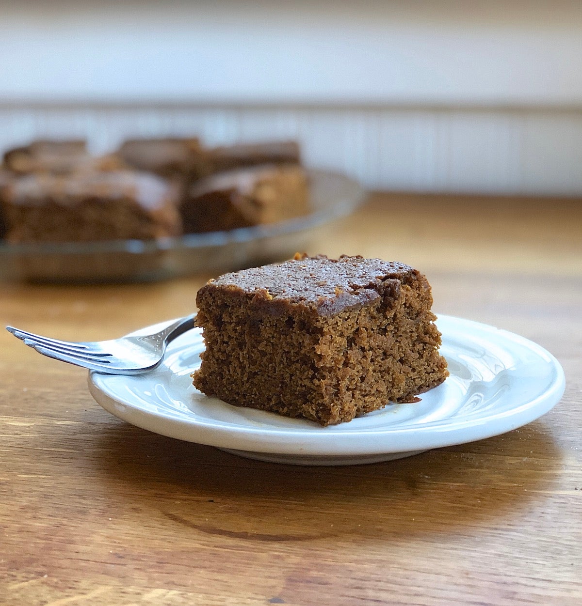 Square of gingerbread on a pewter plate, with fork.